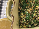 Casserole dish with quinoa topped with parsley and golden raisins next to a sliced lemon
